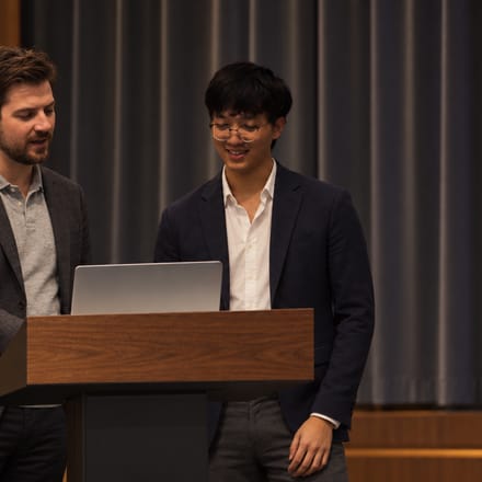 Justin presenting at a lectern with another speaker